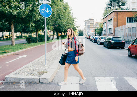Young blonde caucasian woman crossing pedestrian rossing using smart phone - technology, student, social network concept Stock Photo