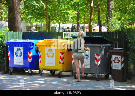 Woman disposing bottles next to a row of recycling bins Stock Photo
