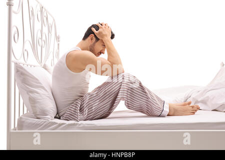 Depressed man sitting on a bed with his head down isolated on white background Stock Photo