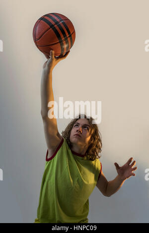 Young boy with long blond hair playing basketball in a striking position with a green jersey on. Stock Photo