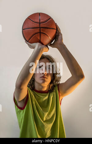 Young boy with blond hair and a green jersey on playing basketball focusing on throwing the ball. Stock Photo