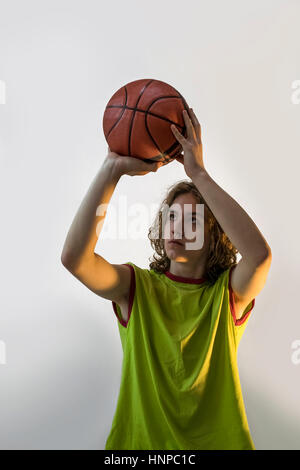 Young boy with blond hair and a green jersey on playing basketball focusing on throwing the ball. Stock Photo