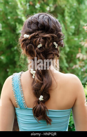 elegant hairstyle with fresh flowers in a plait . Woman with fashion festive hairstyle on nature background. Hairstyle. Wedding, flower decorations in Stock Photo