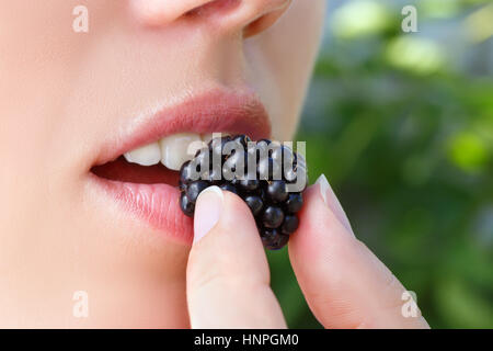 Caucasian woman putting blackberry into mouth closeup. Girl eating blackberries berries. Macro photo. Healthy eating, young woman eating fresh blackbe Stock Photo