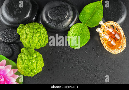 top down of spa concept bergamot, leaf, fragrance oil, lotus and zen stones with water dew on black background, close up Stock Photo