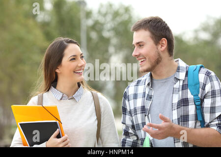 Two happy students walking towards camera and talking in a park or university campus Stock Photo