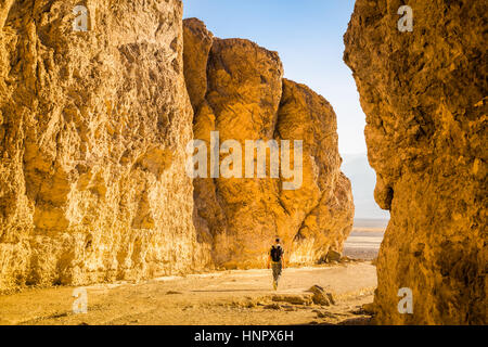 A Male backpacker is hiking on a trail through famous Golden Canyon illuminated in beautiful evening light at sunset in summer, Death Valley NP, USA Stock Photo