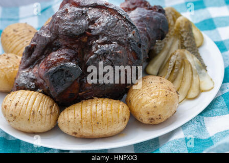 Baked pork knuckle served with potato and pickled cucumbers on a white plate closeup Stock Photo