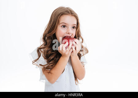 Pretty cutly little girl biting and eating red apple over white background Stock Photo