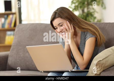 Candid girl watching media content on line in a laptop sitting on a sofa in the living room at home Stock Photo