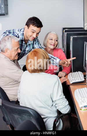 Teacher Assisting Senior People In Using Computer At Classroom Stock Photo