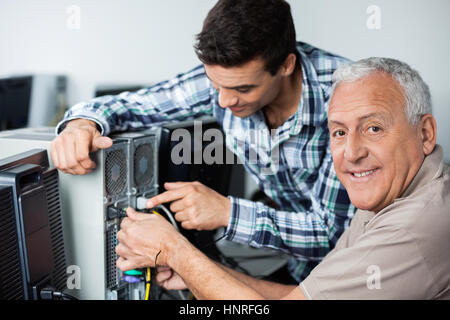 Happy Senior Man With Teacher Installing Computer In Classroom Stock Photo