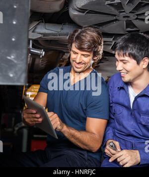 Mechanics Using Digital Tablet Under Car Stock Photo