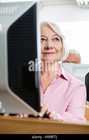 Thoughtful Senior Woman Using Computer In Classroom Stock Photo