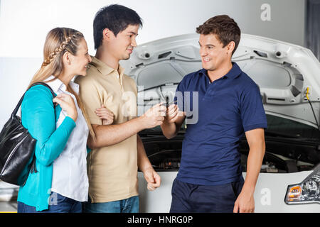 Happy Technician Taking Car Keys From Couple Stock Photo