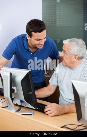 Teacher Looking At Senior Man Using Computer Classroom Stock Photo