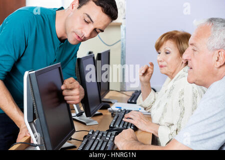 Tutor Guiding Senior Students In Using Computer At Classroom Stock Photo