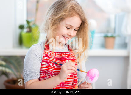 Little blonde girl coloring eggs for Easter holiday at home Stock Photo