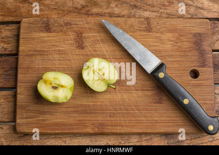 Two halves of an apple and a chef's knife on a wooden cutting board Stock Photo