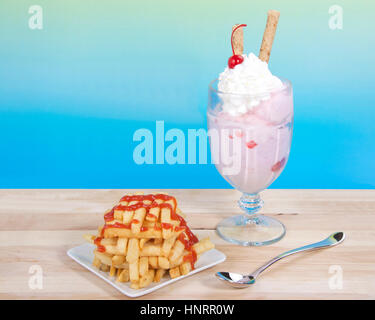 Sweet and Salty. French fries stacked criss crossed on a square plate next to a strawberry sunday ice cream with whipped cream, cherry and pirouette Stock Photo