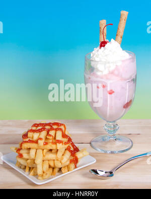 Sweet and Salty. French fries stacked criss crossed on a square plate next to a strawberry sunday ice cream with whipped cream, cherry and pirouette Stock Photo