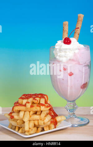 Sweet and Salty. French fries stacked criss crossed on a square plate next to a strawberry sunday ice cream with whipped cream, cherry and pirouette Stock Photo