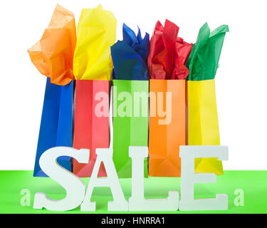 colorful bags with bright tissue paper inserts on a red table with white background and Sale letters. Holiday Sale Stock Photo