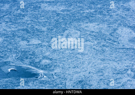 nearly completely frozen glacial lake with intricate patterns and cracks in the ice and blue water Stock Photo