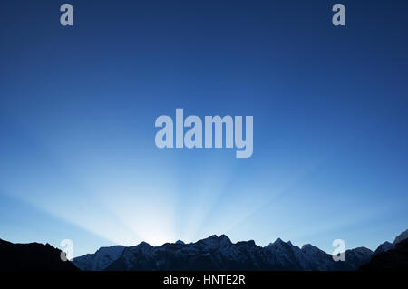 sun rays in a blue sky over mountain peaks Stock Photo