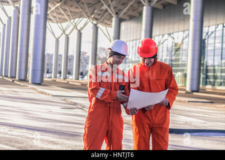 team of  young engineers discussing a construction project and smiling. The wear overalls and safety helmets. Business modern background Stock Photo