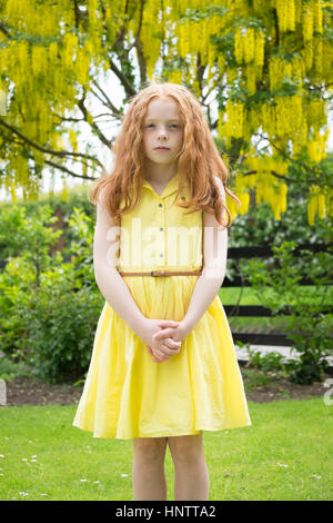 A little girl in  yellow dress standing in front of a yellow tree. Stock Photo