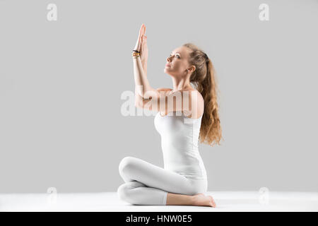 Young woman sitting in Cow Face pose, grey studio background Stock Photo