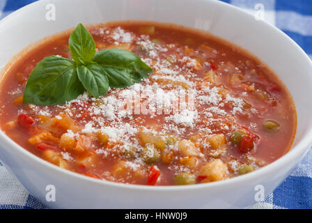Minestrone soup with grated parmesan cheese and basil leaves in a white plate closeup. Stock Photo