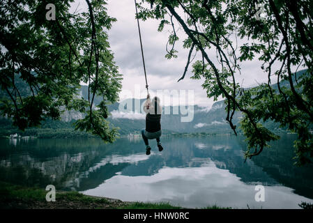 Caucasian woman swinging on rope swing at lake Stock Photo