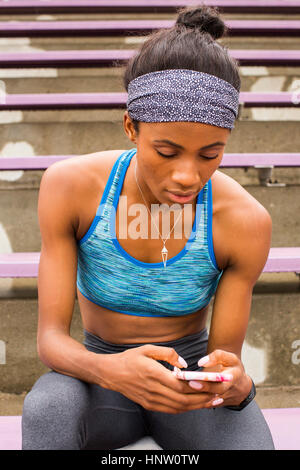 Black woman sitting on bleachers texting on cell phone Stock Photo