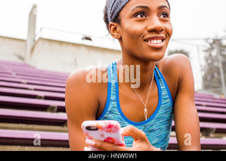 Smiling Black woman sitting on bleachers texting on cell phone Stock Photo