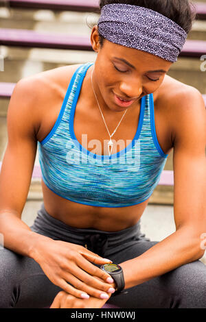 Black woman sitting on bleachers checking smart watch Stock Photo