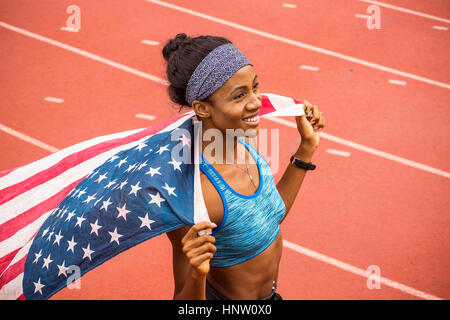 Smiling Black athlete holding American flag on track Stock Photo