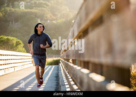 Smiling Mixed Race man running on footbridge Stock Photo