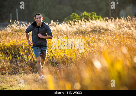 Smiling Mixed Race man running in field Stock Photo