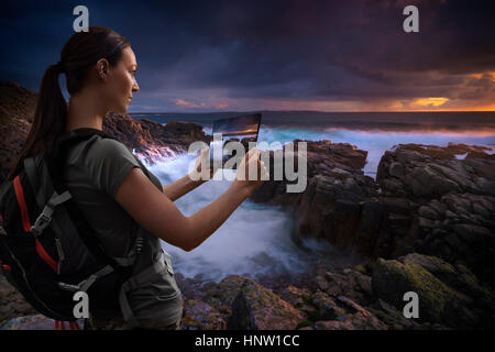 Caucasian woman photographing ocean sunset with digital tablet Stock Photo