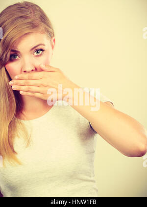 Saying bad things, shocking news concept. Ashamed young blonde woman having hand on her mouth Stock Photo