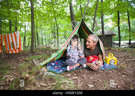 Father watching son playing harmonica in blanket fort Stock Photo