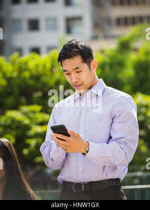 Chinese businessman texting on cell phone outdoors Stock Photo