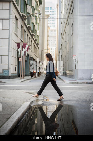 Reflection in puddle of Chinese businesswoman crossing street Stock Photo