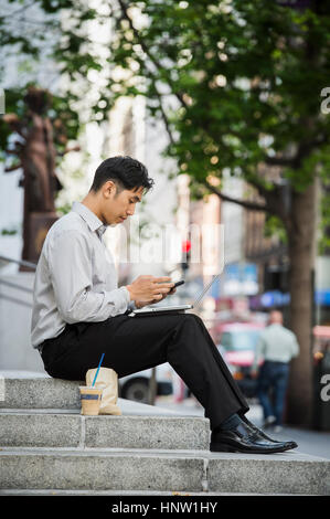 Chinese businessman texting on cell phone during lunch in city Stock Photo