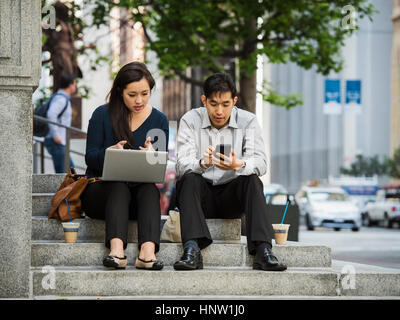 Chinese business people using technology during lunch in city Stock Photo