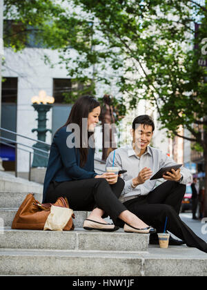 Chinese business people using technology on staircase at lunch Stock Photo