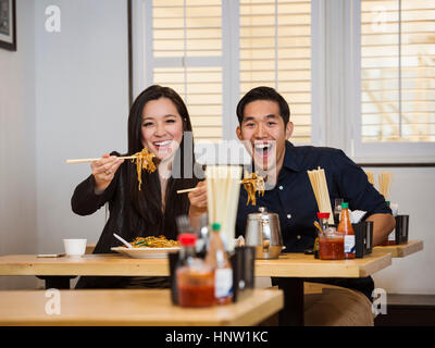 Smiling Chinese couple holding noodles with chopsticks in restaurant Stock Photo