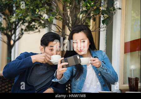 Smiling Chinese couple posing for cell phone selfie at outdoor cafe Stock Photo